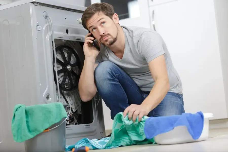 Homeowner on the phone beside a leaking washing machine with towels on the floor