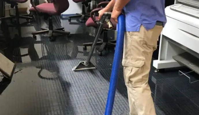 Technician extracting water from wet carpet in a commercial office