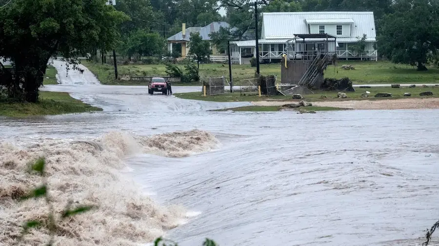 Flash flood water rushing across a road near homes in the Texas Hill Country
