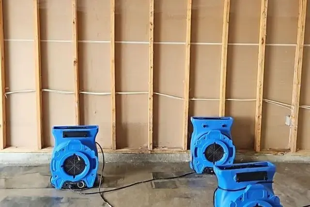 Air movers drying open wall studs and a bare slab after a water loss
