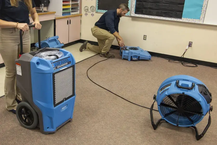 Restoration techs setting a dehumidifier and air mover to dry a room